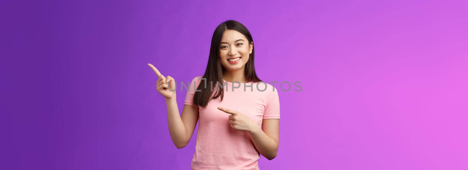 Cheerful friendly tender asian smiling girl pointing right, showing promo, introduce new product, grinning joyfully present cool adverstiment, stand pink t-shirt purple background amused outgoing by Benzoix