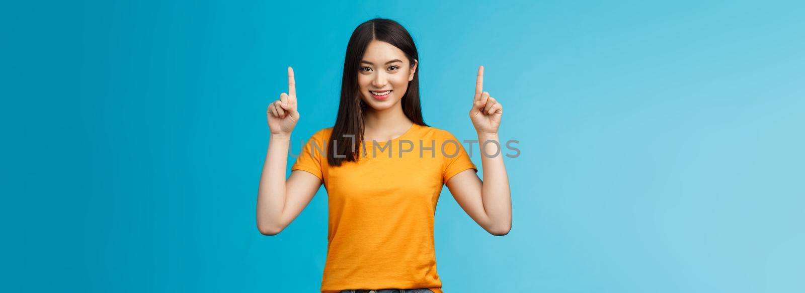 Cheerful cute young urban korean girl introduce new product, show promo, pointing raised fingers up advertisement, smiling joyfully, satisfied toothy grin, give recommendation what choose.