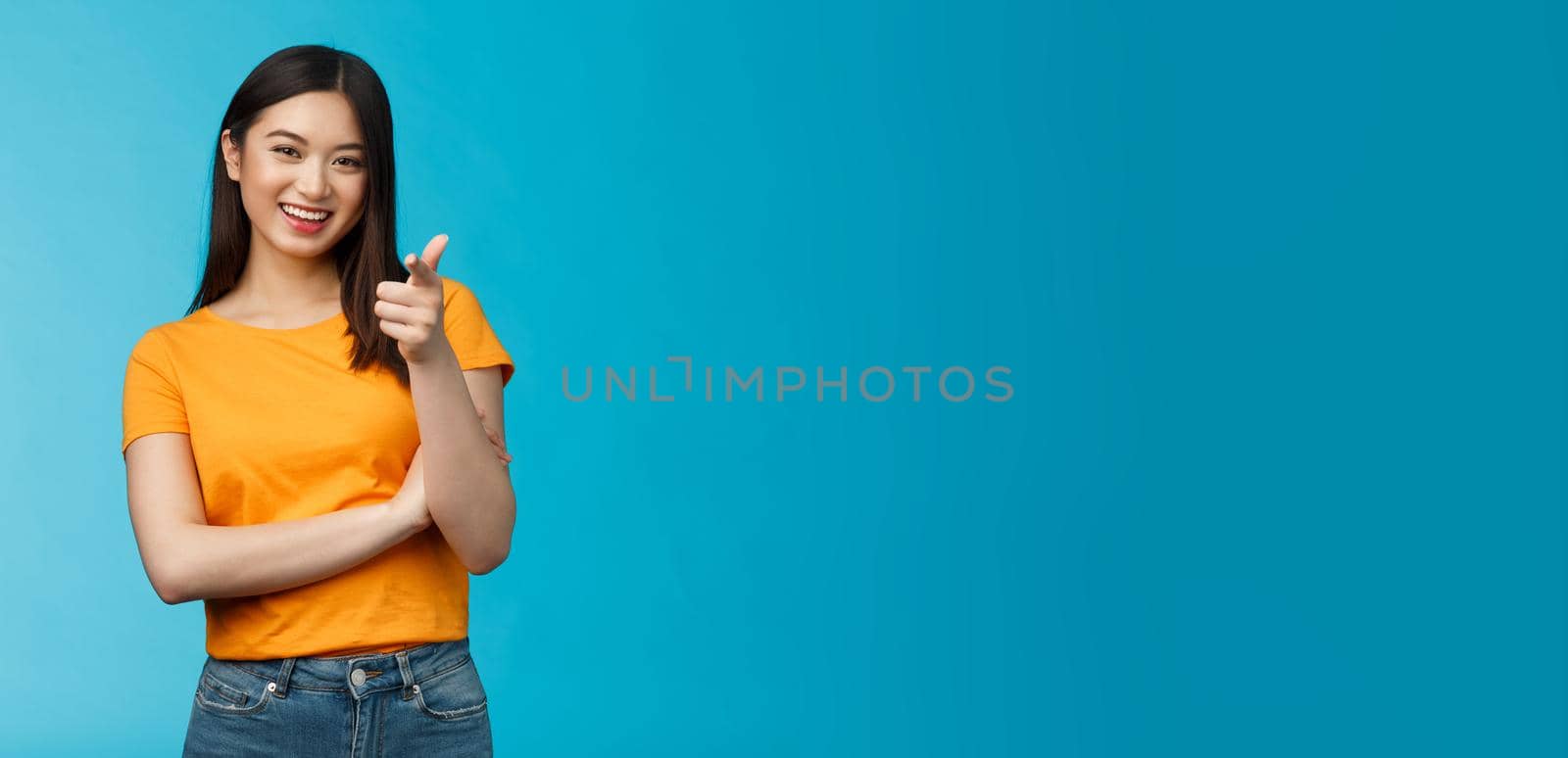 Hey you got point. Cheerful cute asian lively girl dark short haircut pointing camera finger-pistol smiling broadly, encourage friend make move, congratulate coworker good job, stand blue background by Benzoix