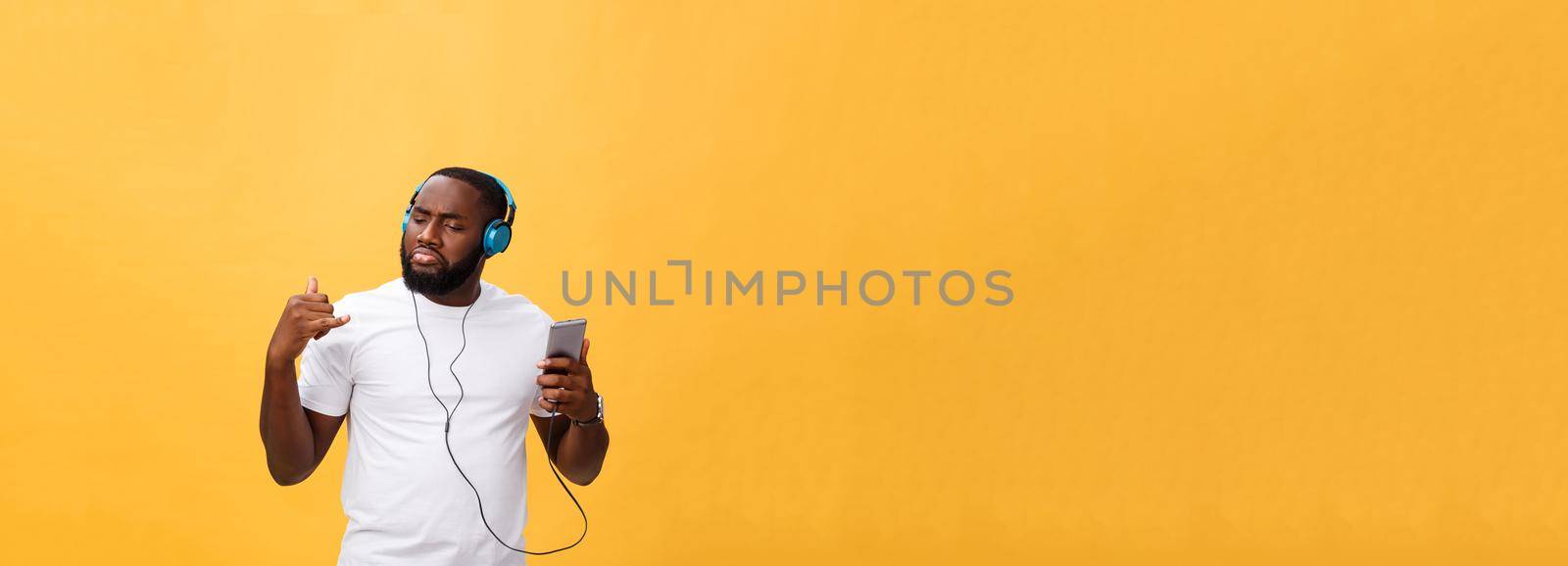 African American man with headphones listen and dance with music. Isolated on yellow background.