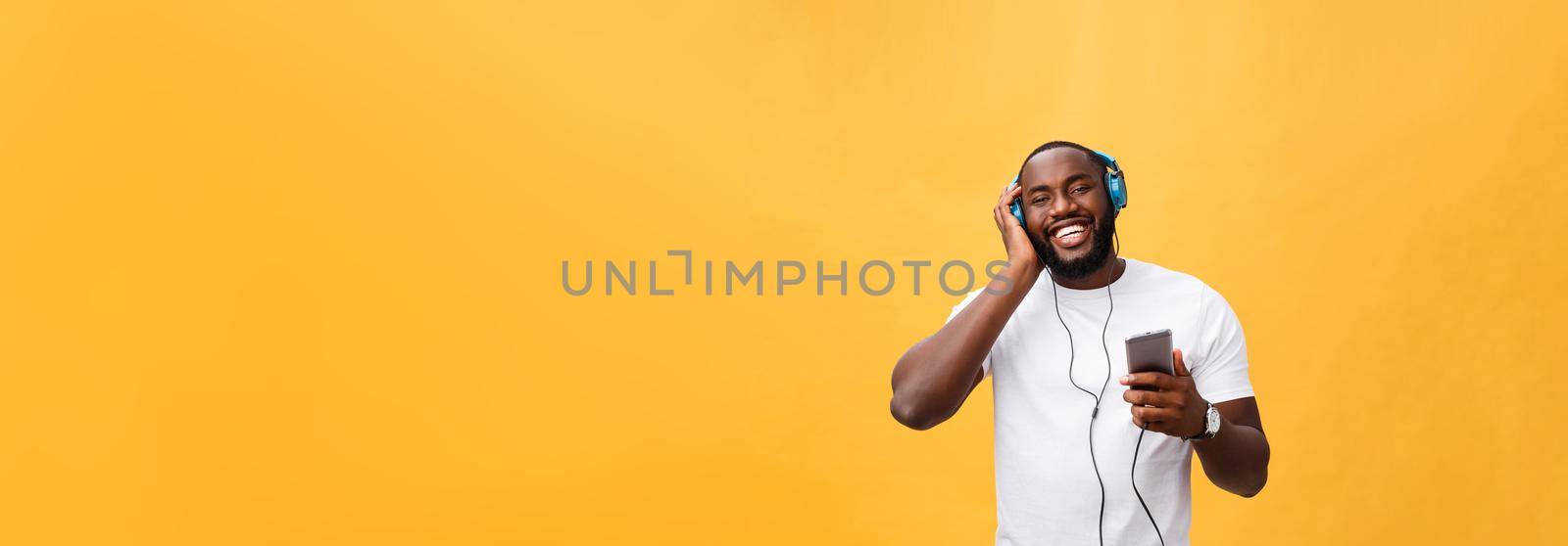 Young African American man wearing headphone and enjoy music over yellow gold Background.