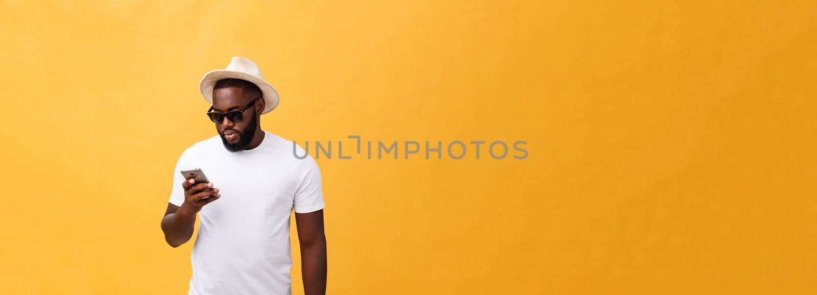 Cheerful African American man in white shirt using mobile phone application. happy dark skinned hipster guy read news from social network in mobile phone. by Benzoix