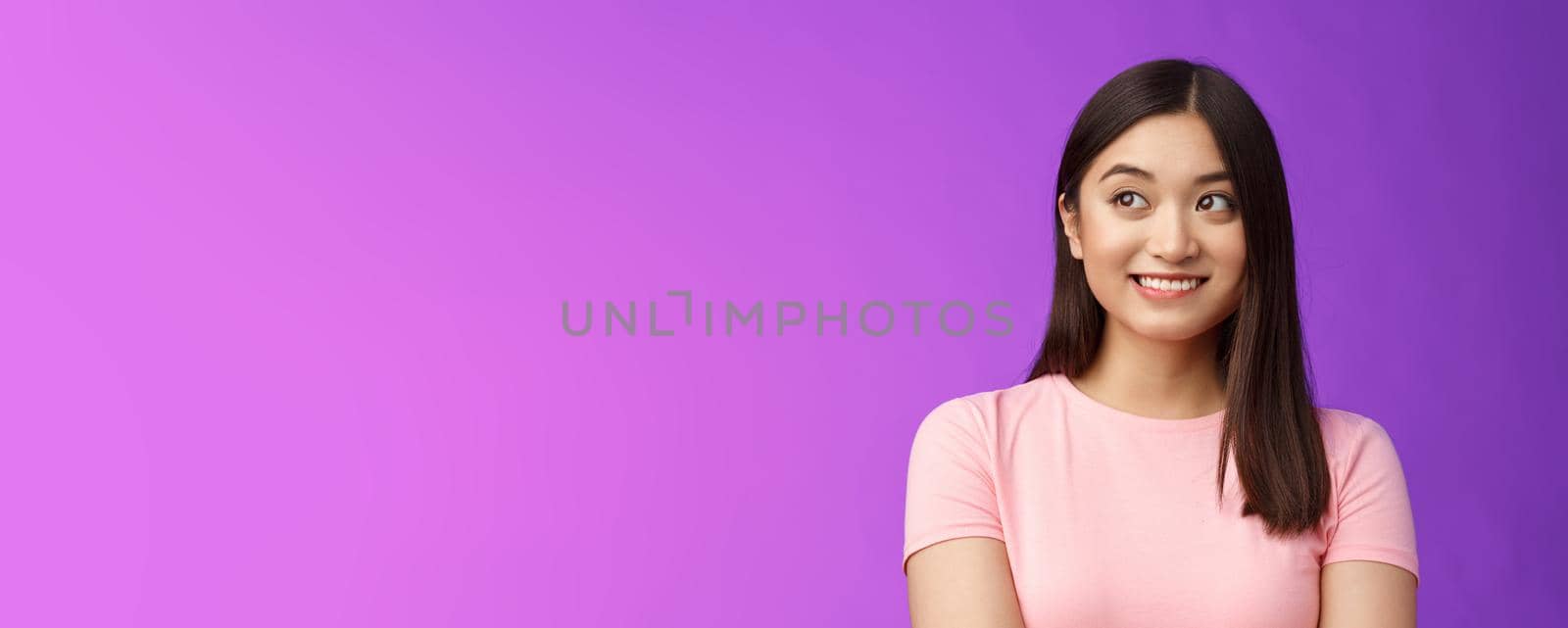 Close-up lovely joyful asian woman look away dreamy, smiling imaging cute thing, recall funny joke, thinking happy moment, stand modest purple background upbeat and silly. Copy space