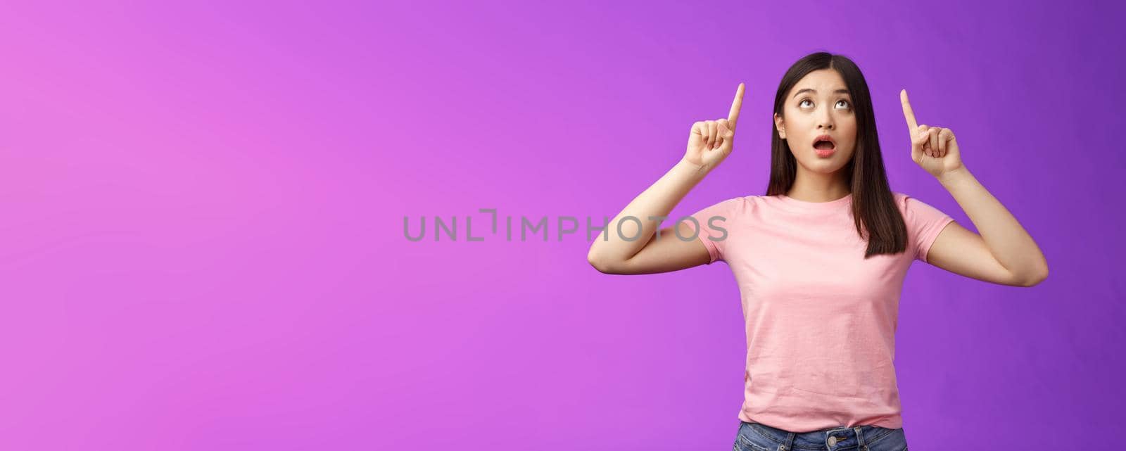 Surprised impressed asian girl brunette look fascinated up, drop jaw gasping astonished, check out impressive interesting promo, pointing top advertisement amazed, stand purple background.