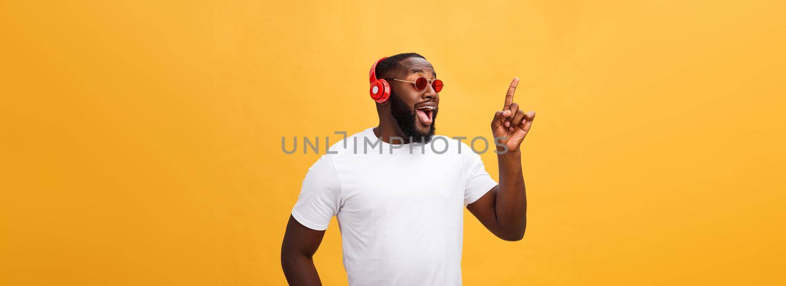 Handsome young African American man listening and smiling with music on his mobile device. Isolated over yellow background