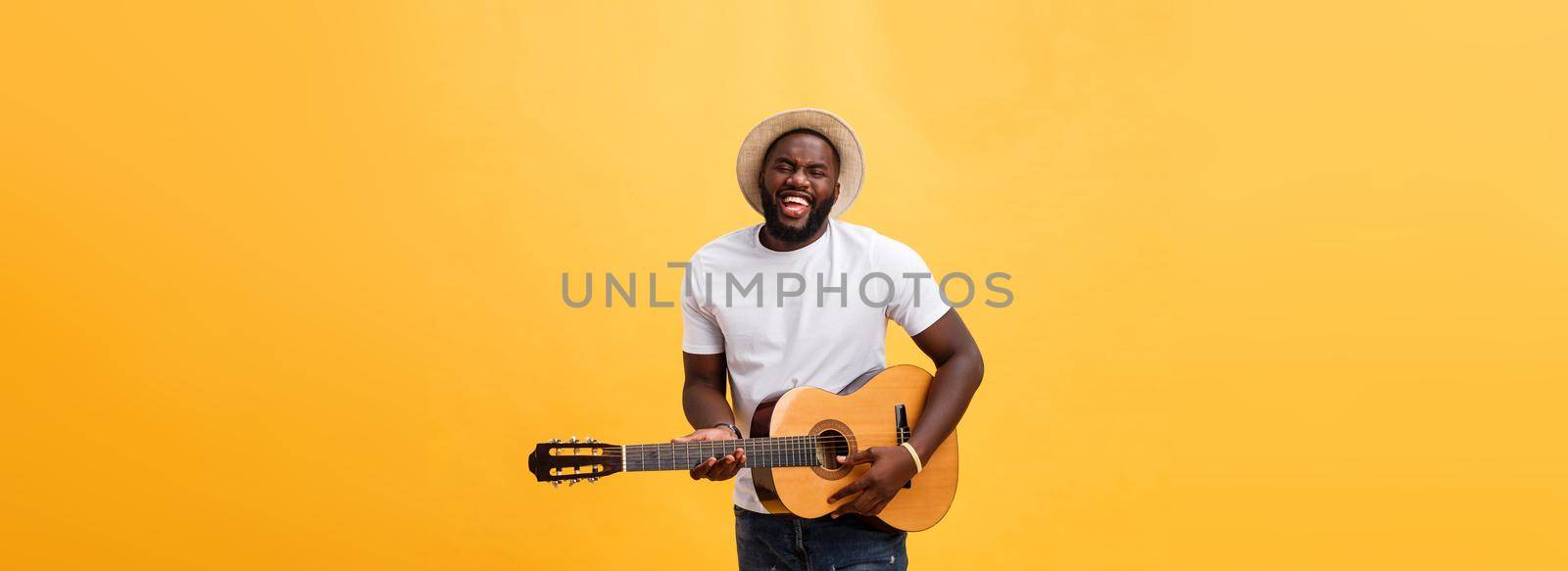 Handsome african american retro styled guitarist playing acoustic guitar isolated on yellow background