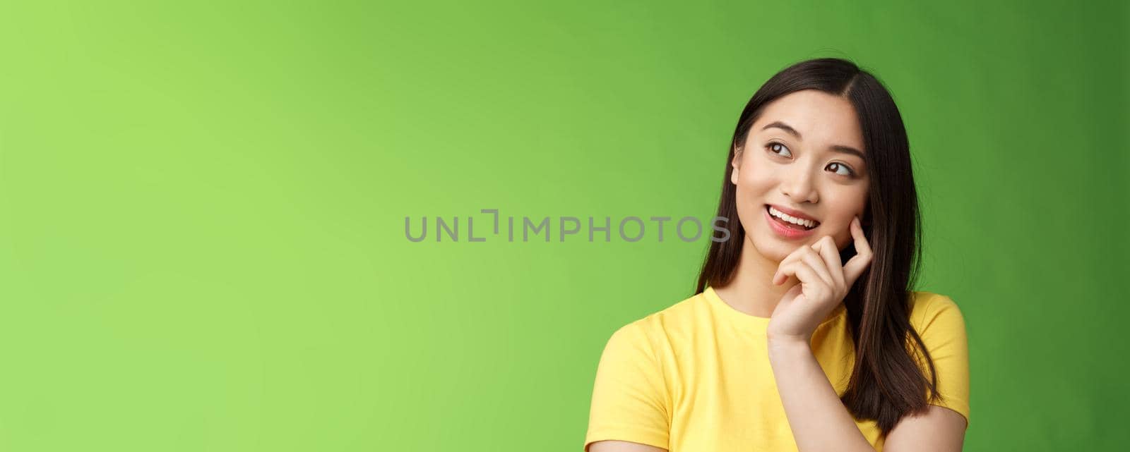 Close-up dreamy intrigued creative asian brunette woman imaging summer vacation trip, picturing perfect holiday, standing thoughtful, touch cheek, thinking look up, stand green background.