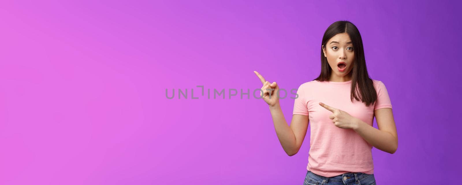 Shocked upset speechless cute asian girl react stunned friend got expensive car, drop jaw astonished, look camera full disbelief, pointing left, discuss astonishing news, stand purple background.