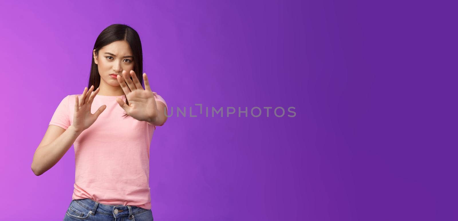 Displeased intense reluctant asian girl blocking, trying protect face, raise hands stop, prohibition gesture, frowning sulking, refusing bothering offer, stand purple background, rejecting.