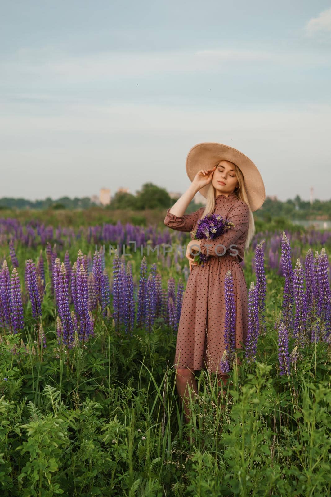 A beautiful woman in a straw hat walks in a field with purple flowers. A walk in nature in the lupin field.