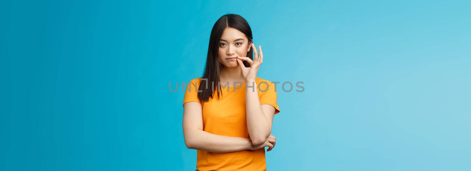 Serious-looking asian female friend promise keep secret, seal lips, hold zip near mouth look focused determined, stay silent and speechless, stand wearing yellow t-shirt blue background by Benzoix