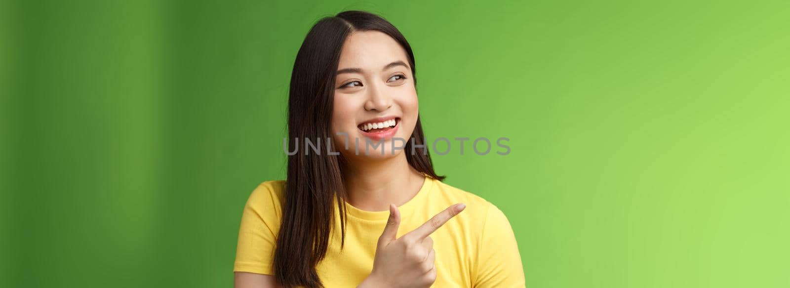 Friendly ougoing cute asian girl having funny conversation, joyfully turn pointing left, indicate awesome cool object, discuss interesting event, chatting carefree, stand green background by Benzoix