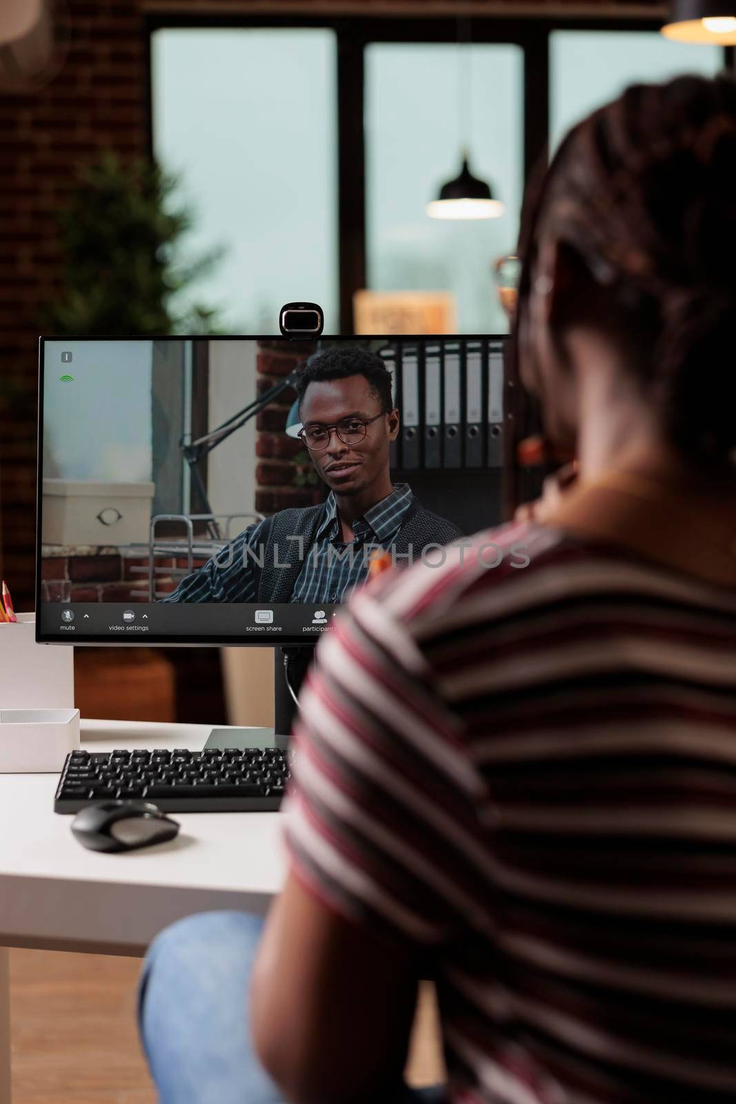 Freelancer talking with client on videoconference, back view, focus on computer monitor. Woman working from home, employee attending virtual meeting, online videocall communication