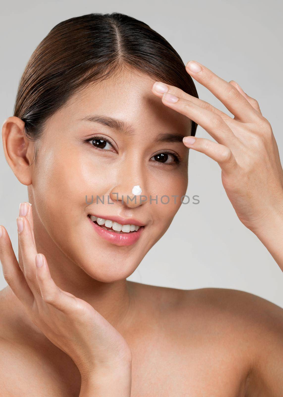 Closeup ardent girl with soft makeup applying moisturizing cream on her nose. by biancoblue