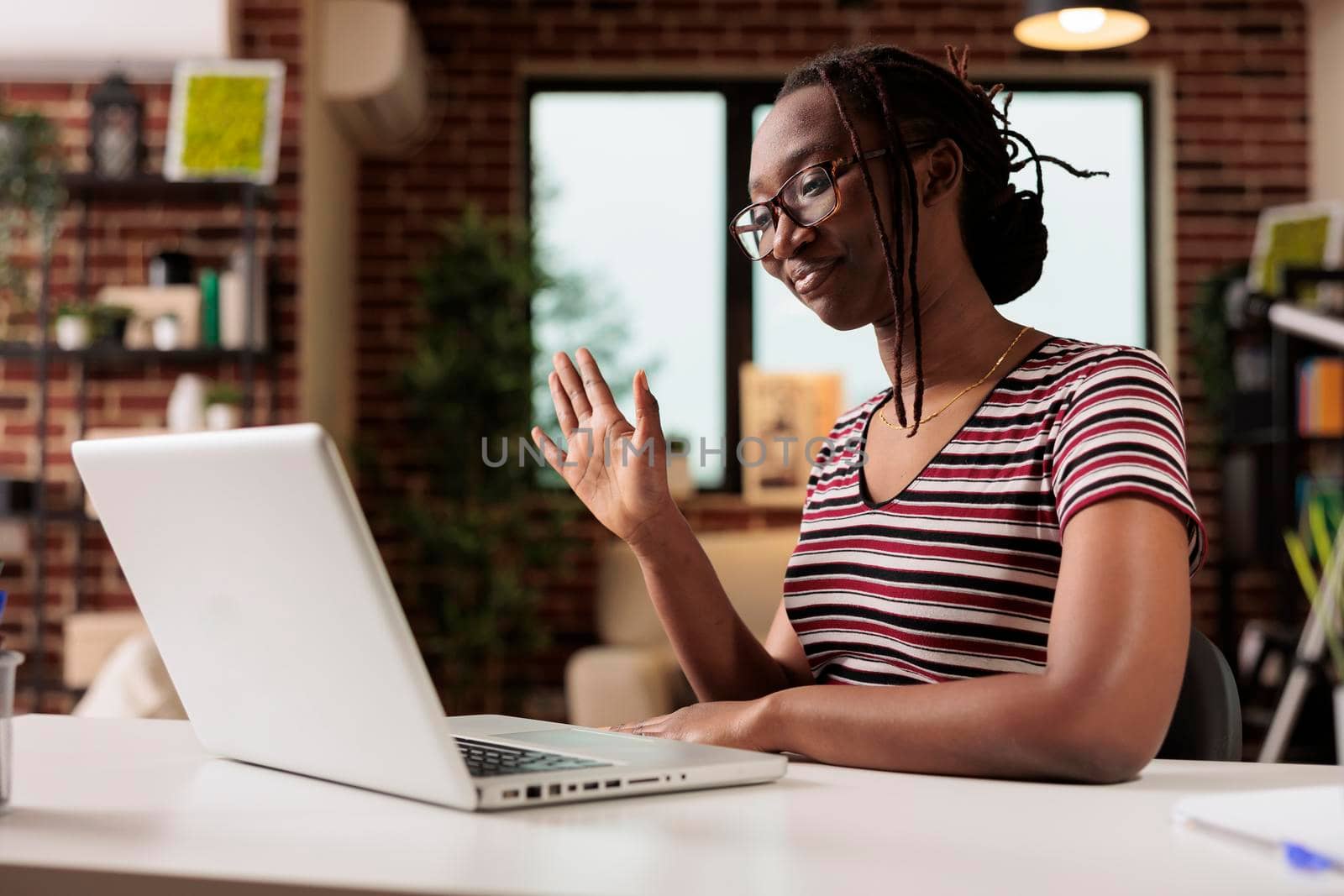 Smiling young freelancer greeting client on videocall interview, woman working on laptop in home office. Employee attending virtual meeting, looking at computer camera, waving hi