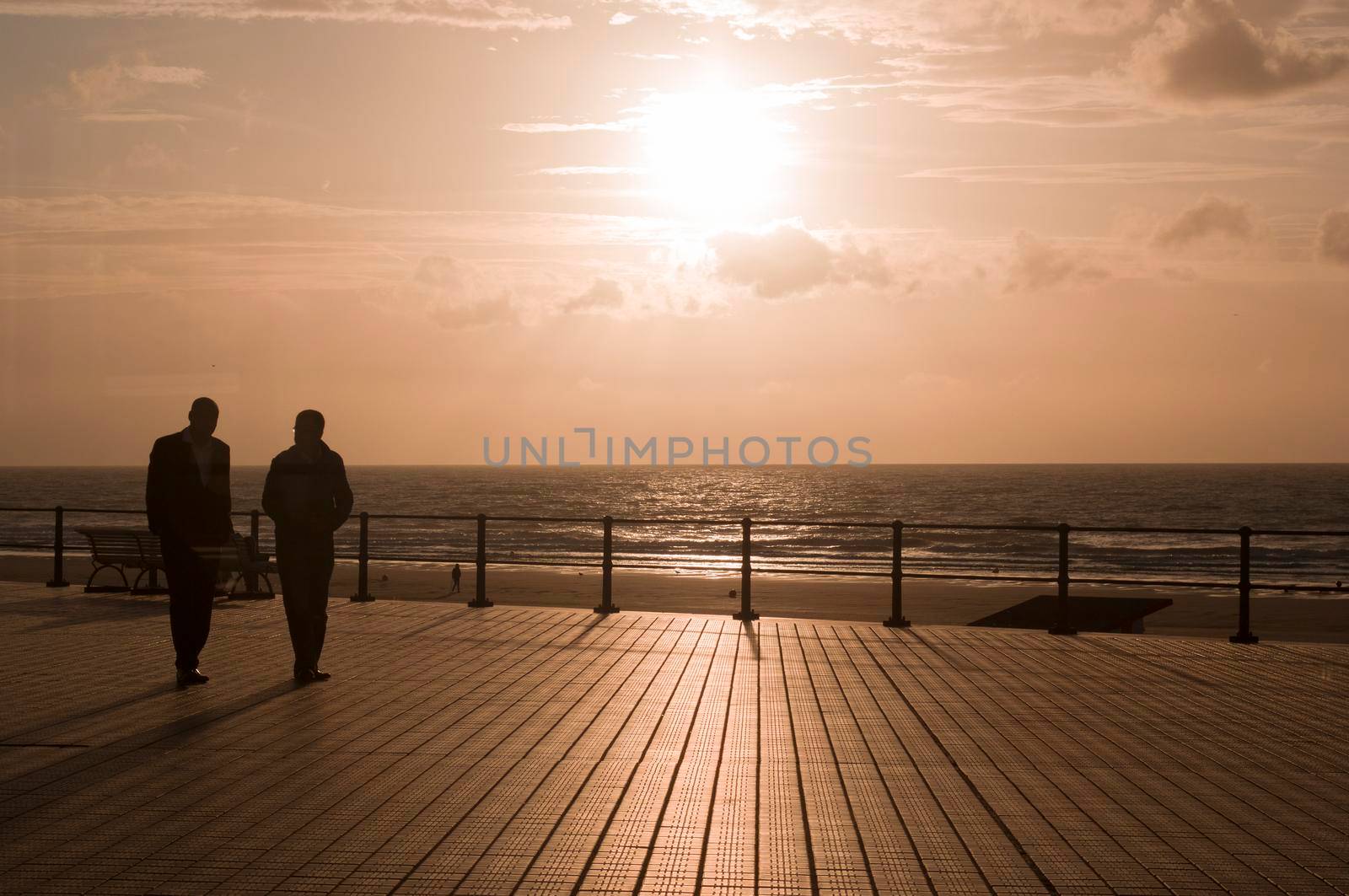 a pair of male friends walking along the terrace against the background of the sunset silhouettes of people. High quality photo