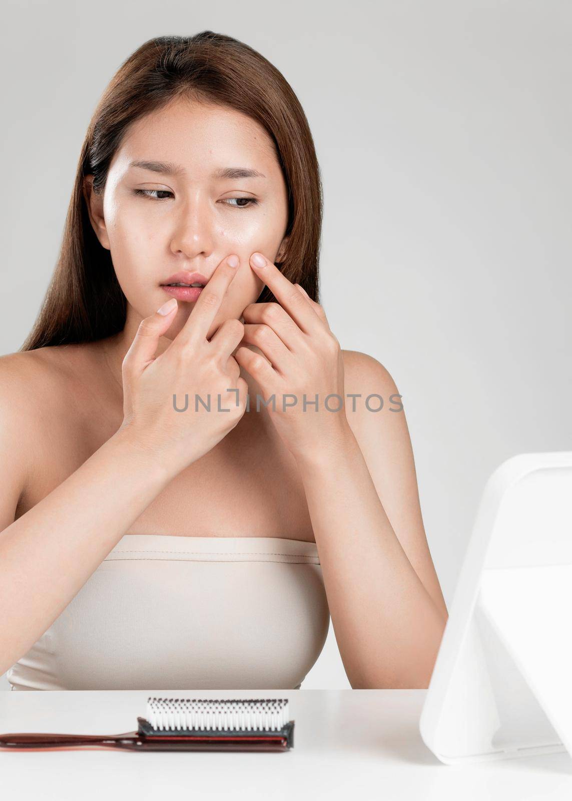 Portrait of young ardent asian woman looking in the mirror worry about pimple on her face. Beauty care for skin problem, acne treatment concept.