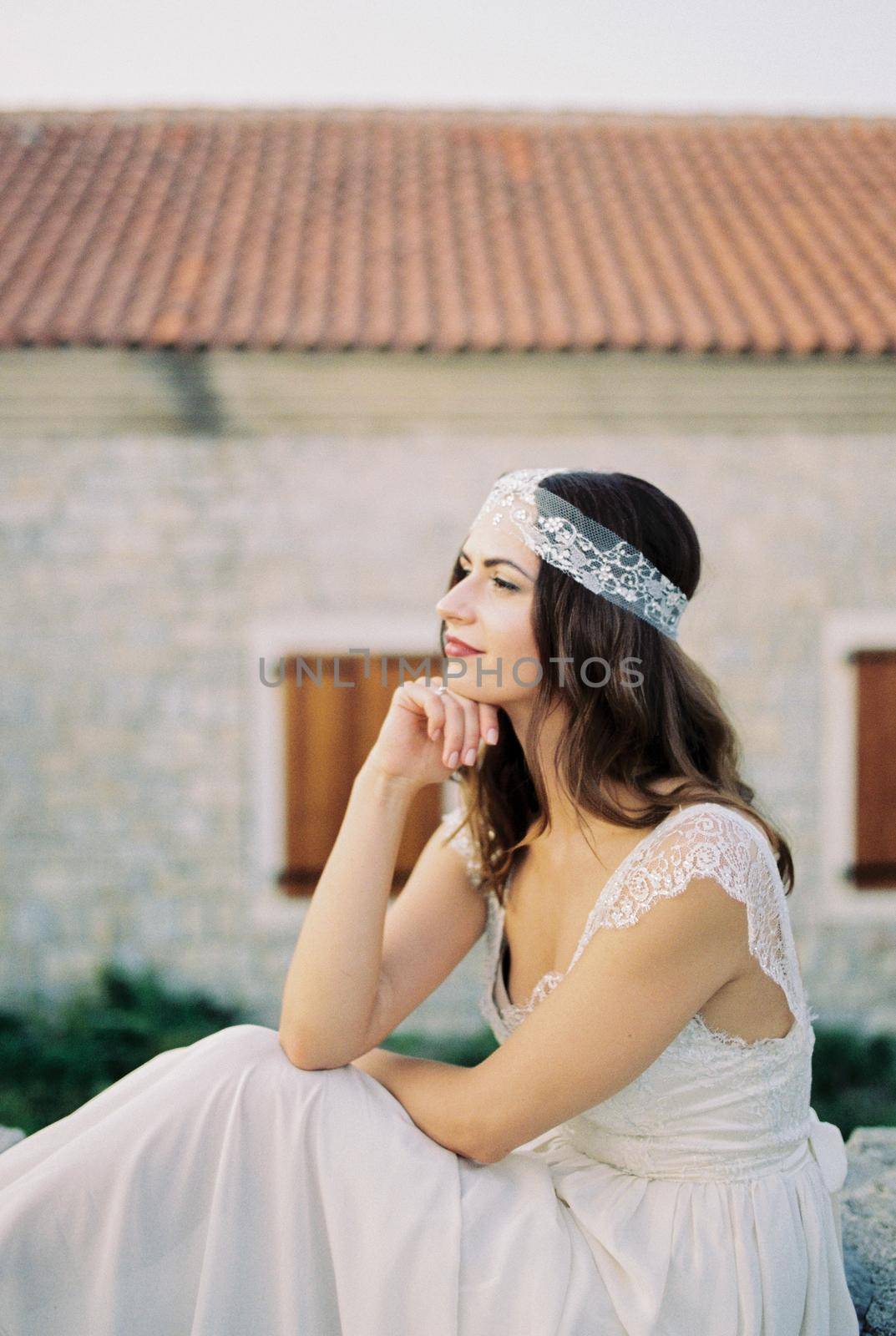 Bride sits against the backdrop of an old building, resting her chin on her hand. High quality photo