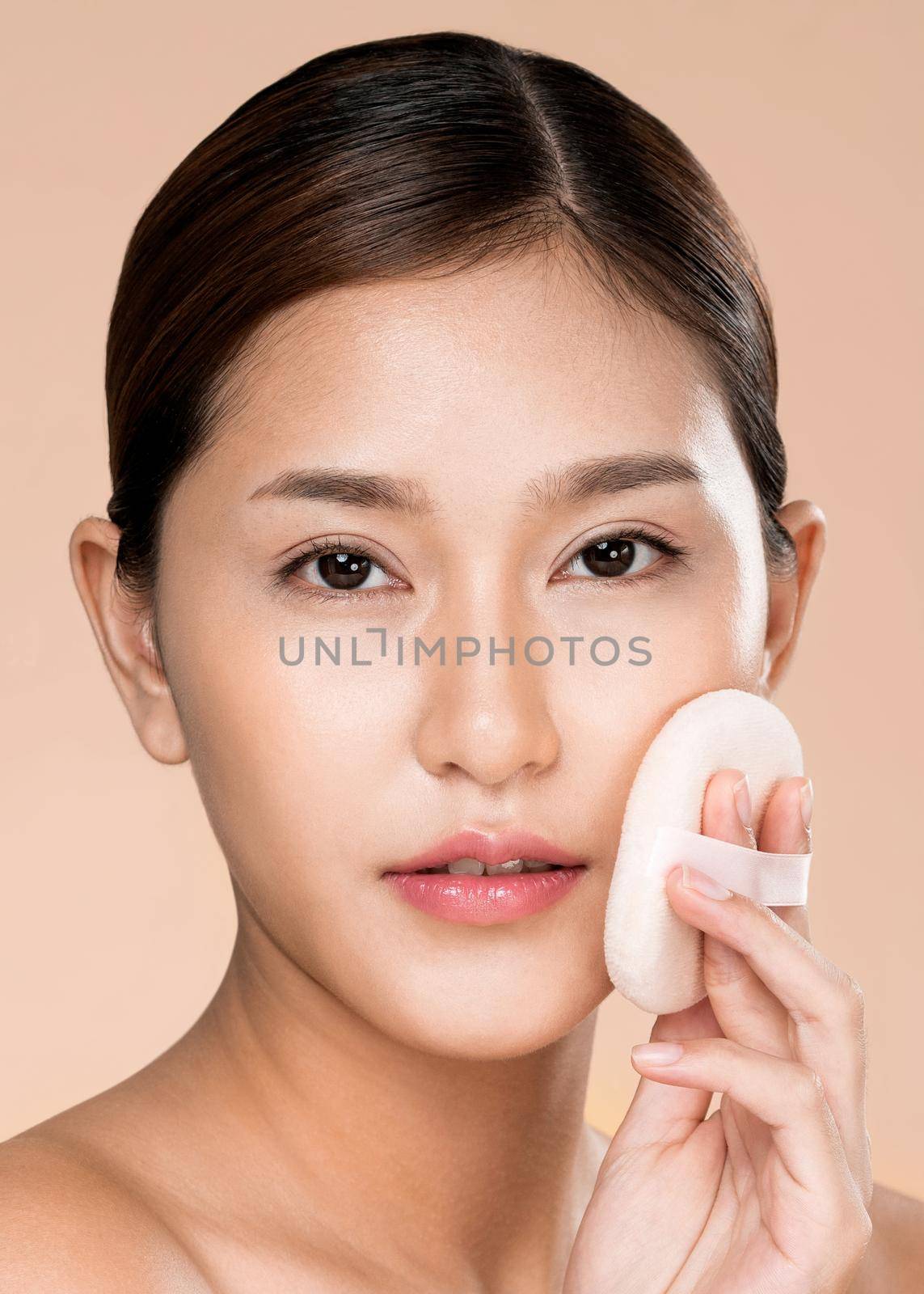 Closeup ardent woman applying her cheek with dry powder while looking at camera. by biancoblue