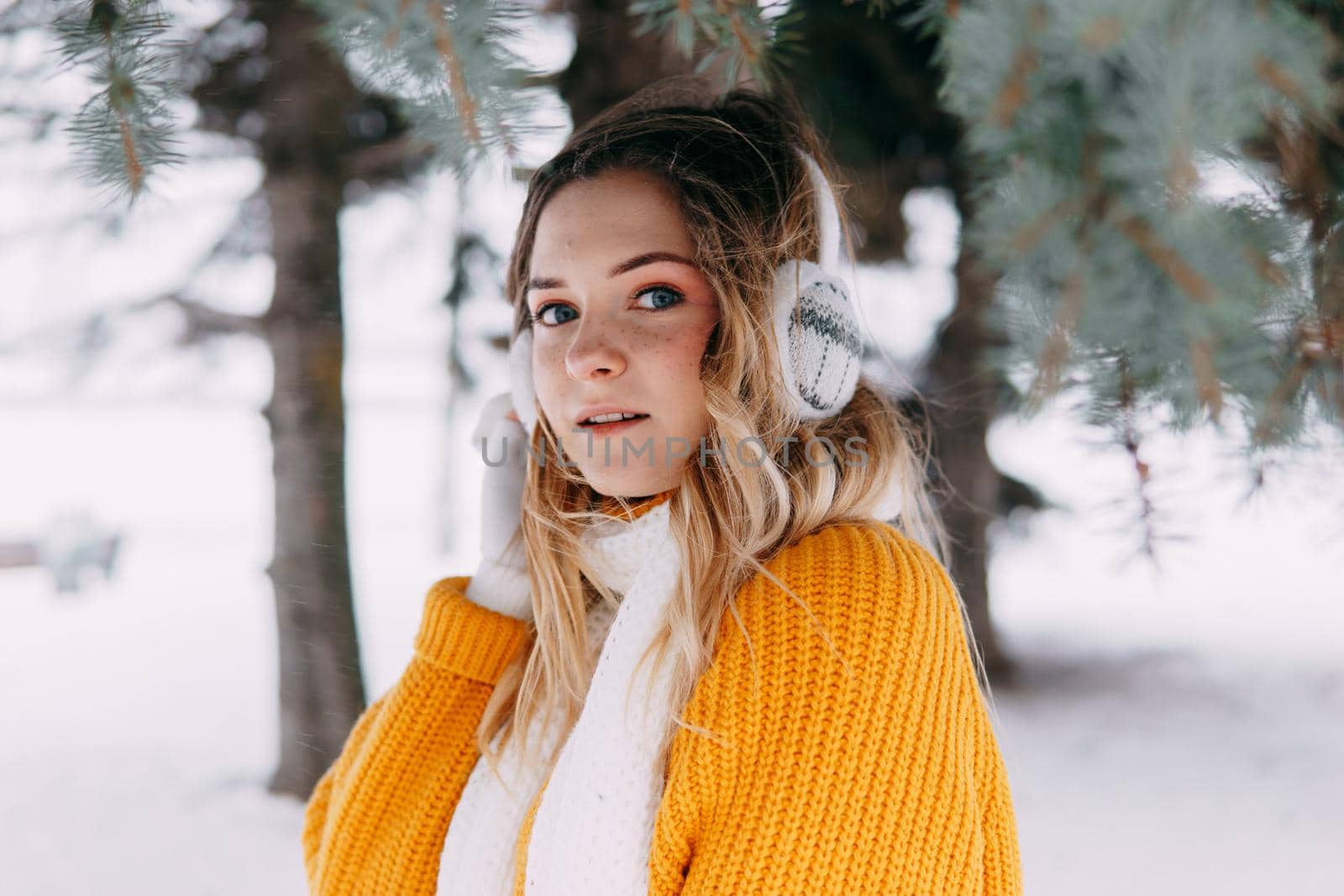 Teen blonde in a yellow sweater outside in winter. A teenage girl on a walk in winter clothes in a snowy forest.