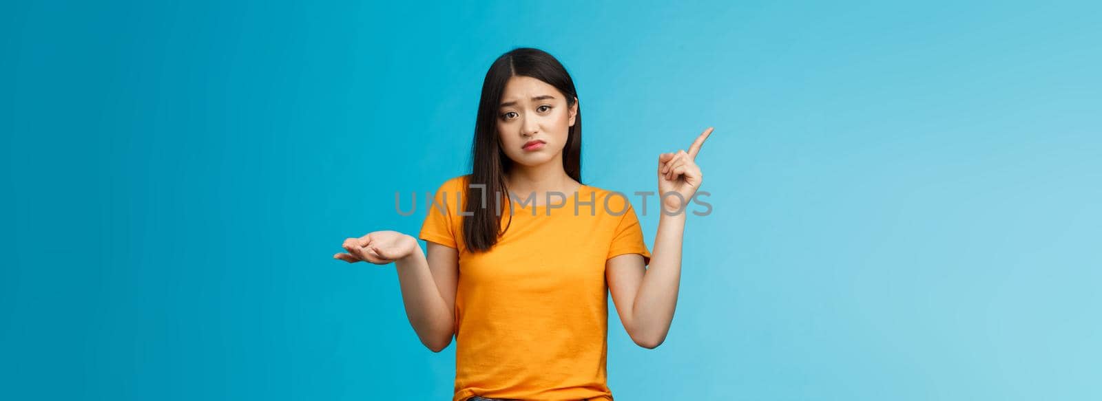 Troubled cute upset asian girl have problem asking your help, pointing upper left corner shrugging unsure, look frustrated and sad, questioned answer, cannot deal problem, stand blue background by Benzoix