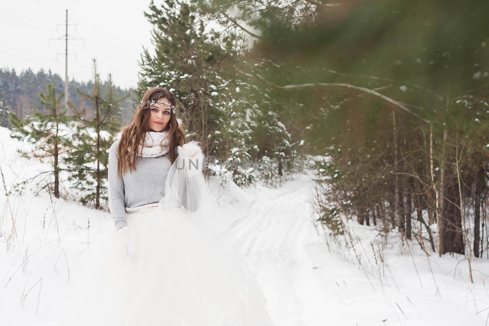 Beautiful bride in a white dress with a bouquet in a snow-covered winter forest. Portrait of the bride in nature.