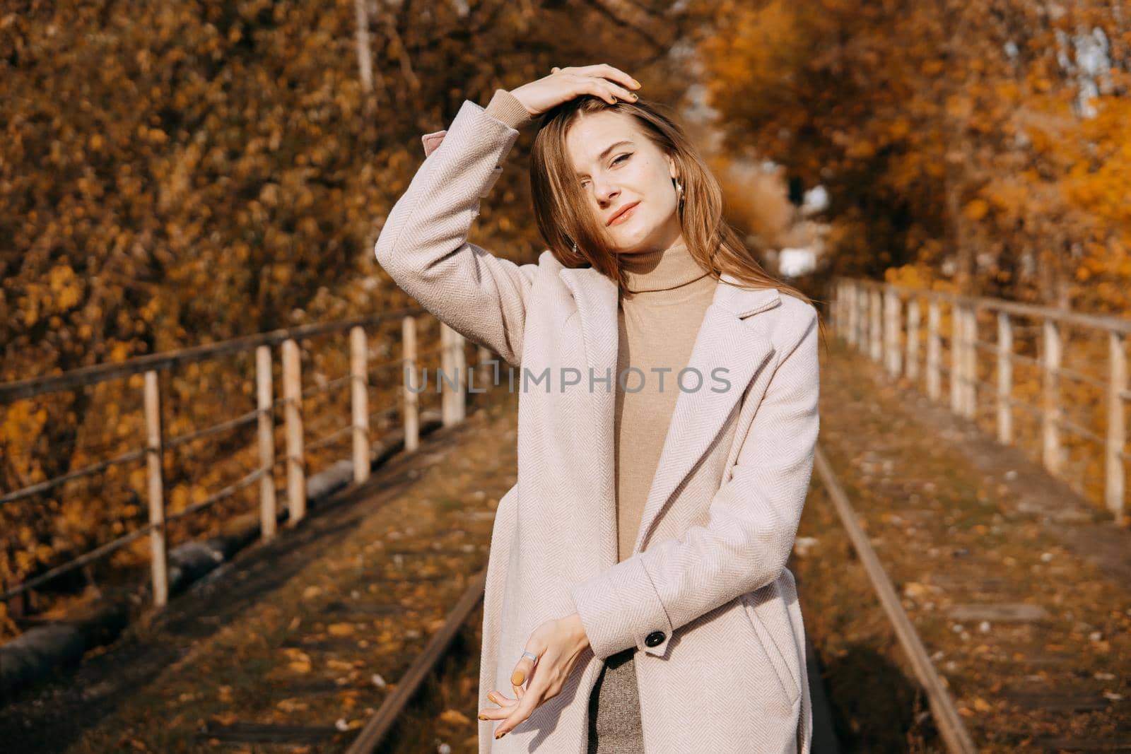 A beautiful long-haired woman walks through the autumn streets. Railway, autumn leaves, a woman in a light coat.