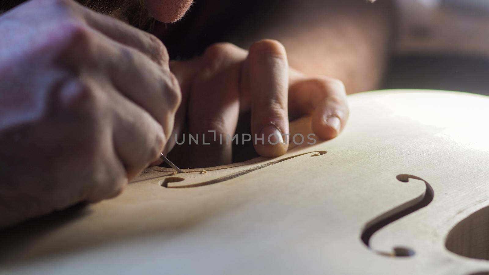 Close up of professional master artisan luthier painstaking detailed work on wood violin in a workshop.