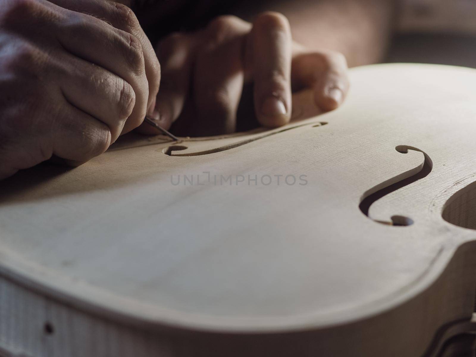 Close up of professional master artisan luthier painstaking detailed work on wood violin in a workshop.