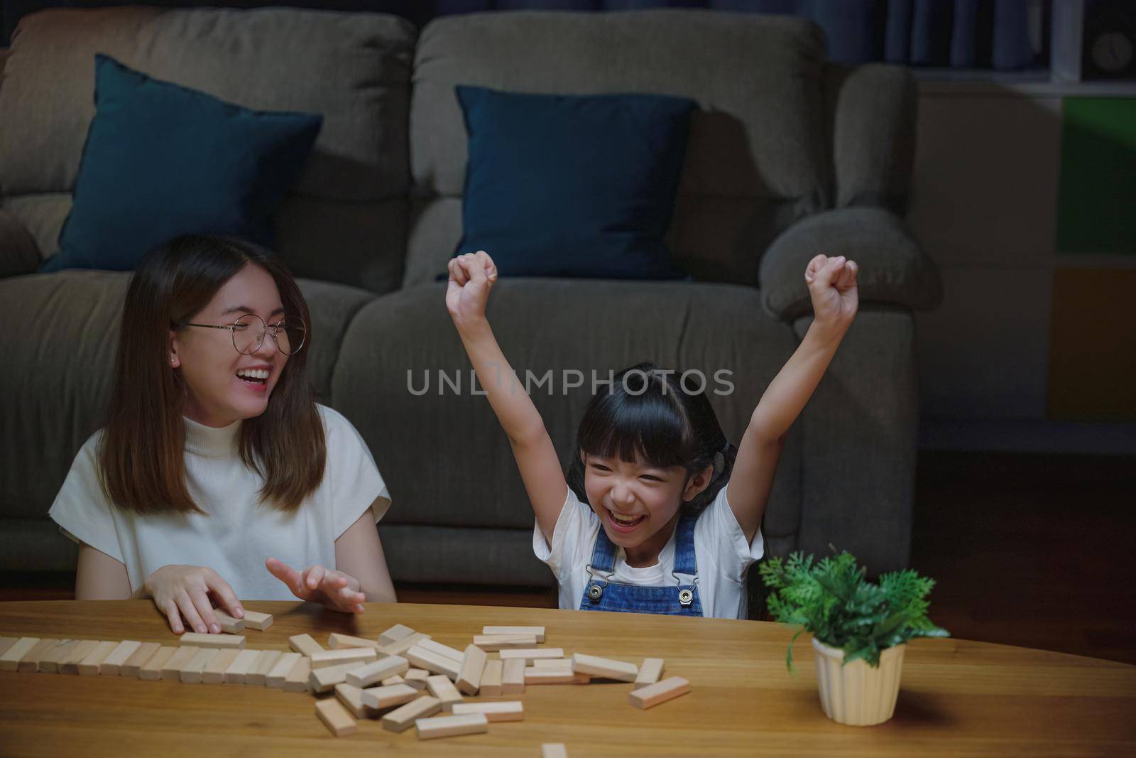 Asian young mother playing game in wood block with her little daughter in home living room at night time, Smiling woman help teach child play build constructor of wooden blocks, education