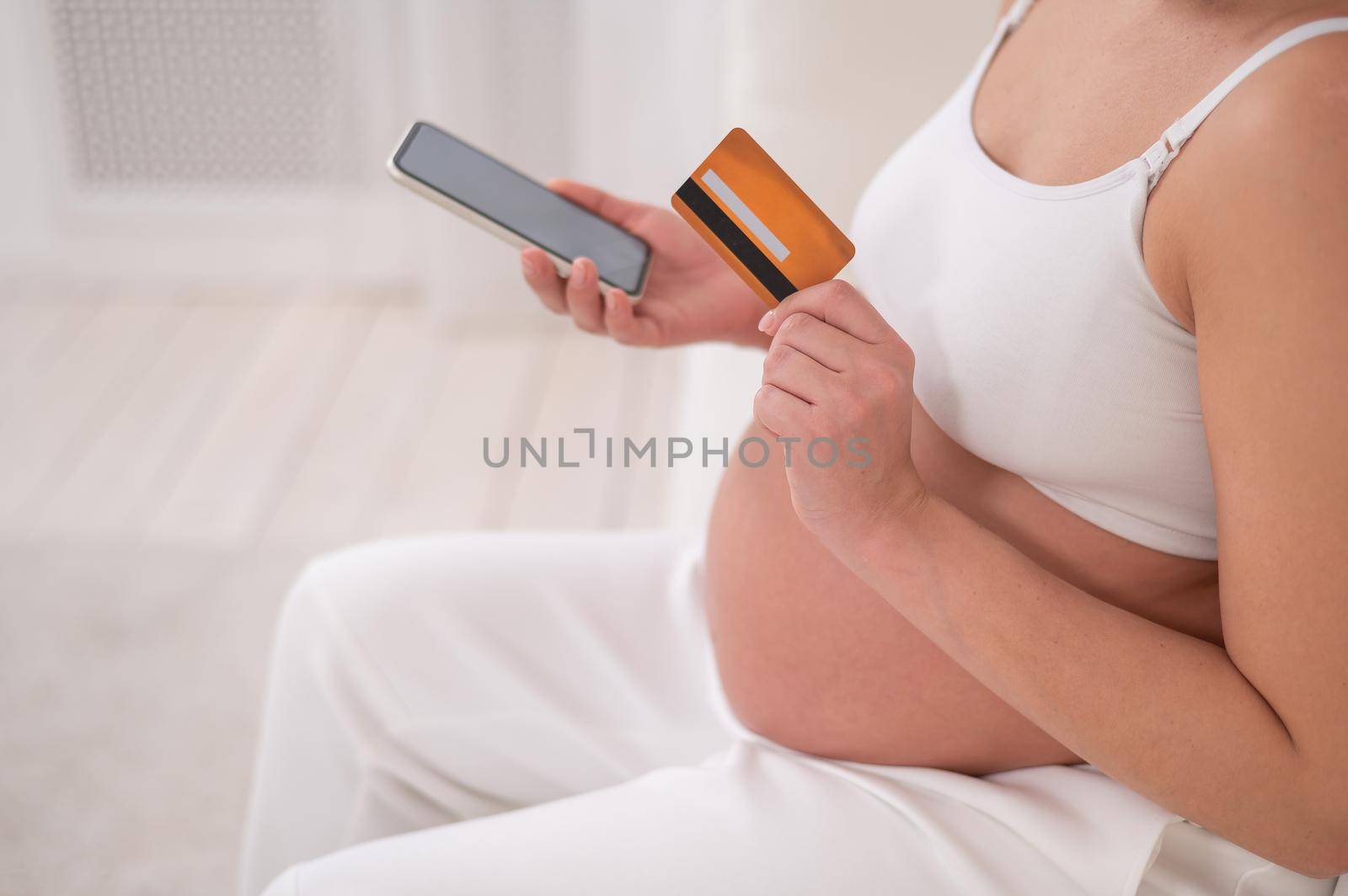 A pregnant woman is holding a smartphone and a credit card. Online shopping concept. by mrwed54