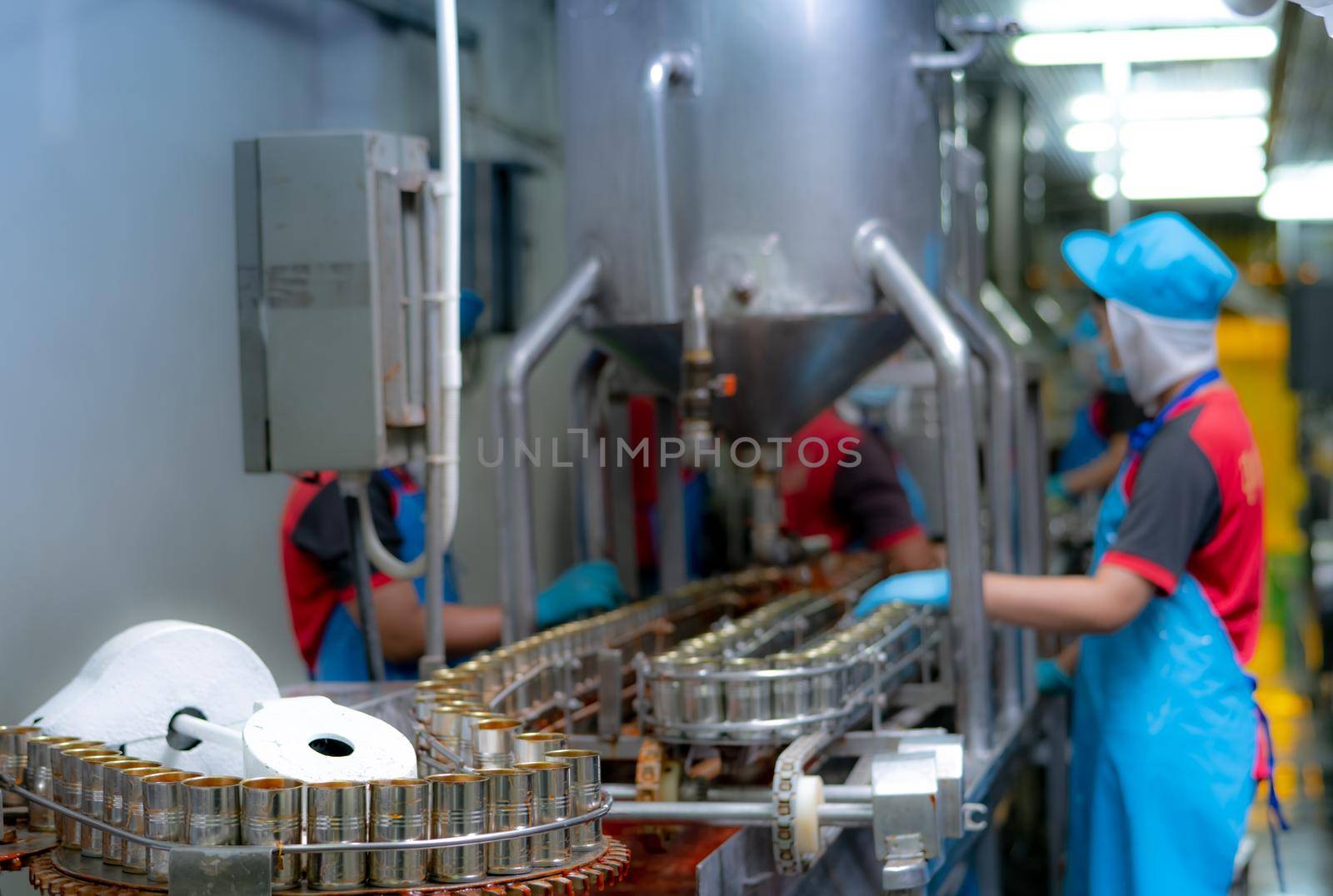 Canned fish factory. Food industry.  Sardines in red tomato sauce in tinned cans on conveyor belt at food factory. Blur workers working in food processing production line. Food manufacturing industry. by Fahroni