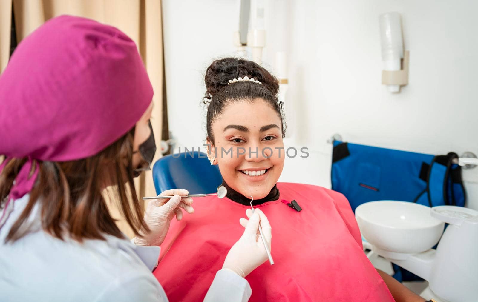 Professional dentist examining female patient in office. Close up of smiling patient at dentist's office looking at camera, Smiling patient in dentist's chair