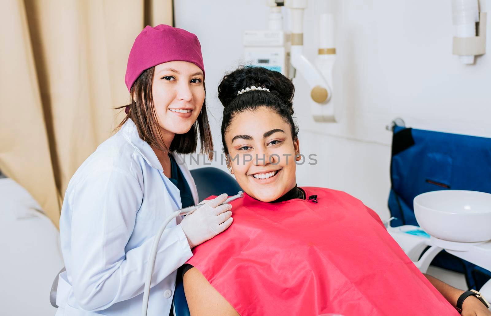 Female dentist with smiling female patient looking at camera, Professional dentist with female patient in office, Portrait of smiling dentist with female patient in medical office by isaiphoto