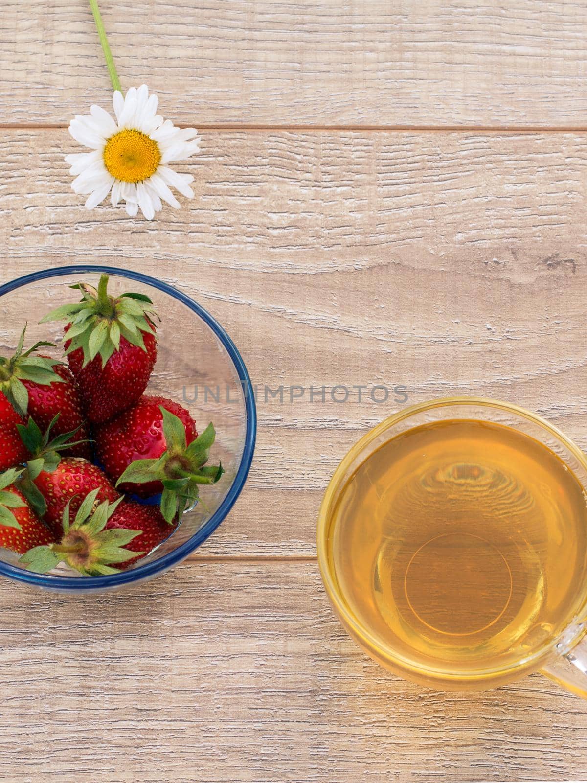 Glass cup of green tea, chamomile flower, glass bowl with fresh strawberries on the wooden boards. Top view.