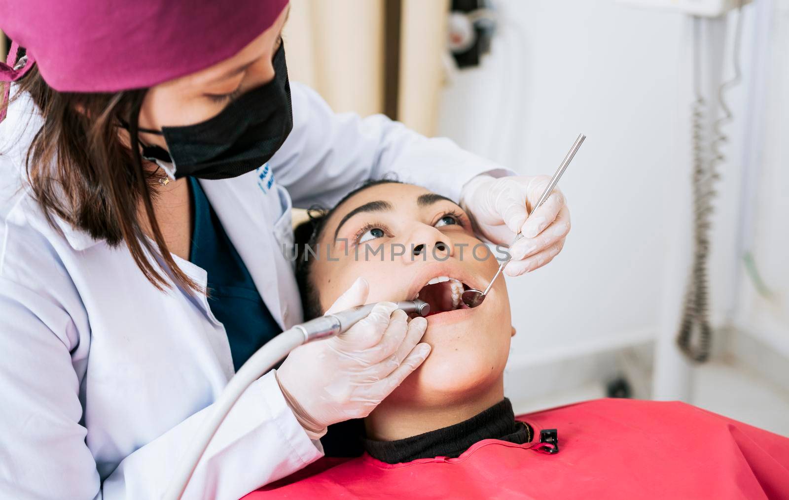 Female dentist cleaning and examining a female patient mouth. Dental specialist cleaning the teeth of a female patient. Professional dentist cleaning a female patient's mouth