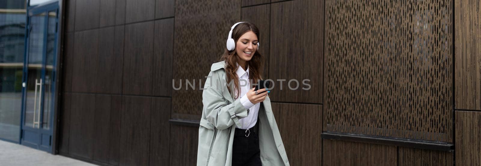 young stylish HR manager walking down the street in headphones next to the business center.