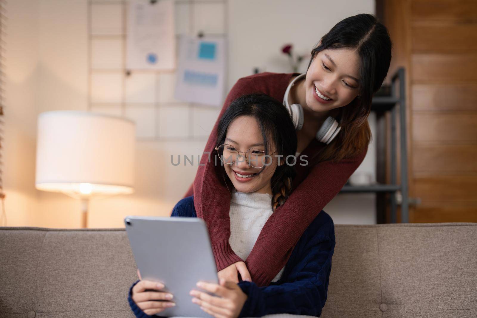 Two asian women having nice lively activity in living room on sofa in cozy interior.