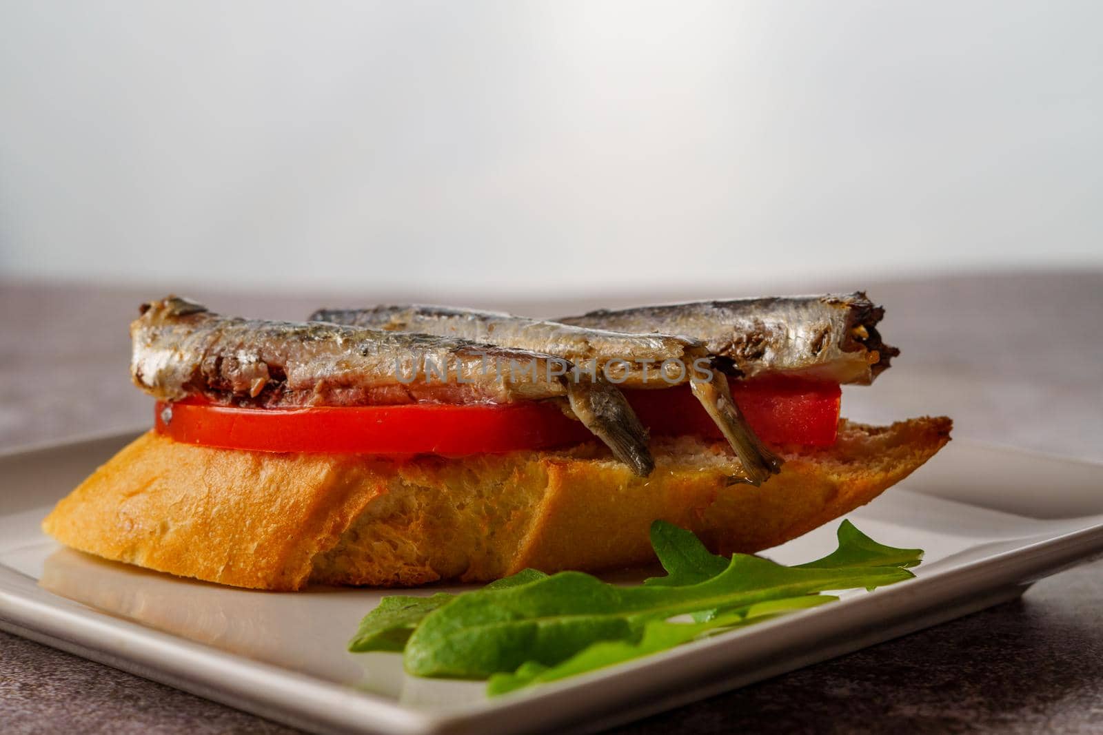 tapa of sardines on a slice of bread with tomato and olives on a white plate with a typical spanish white background