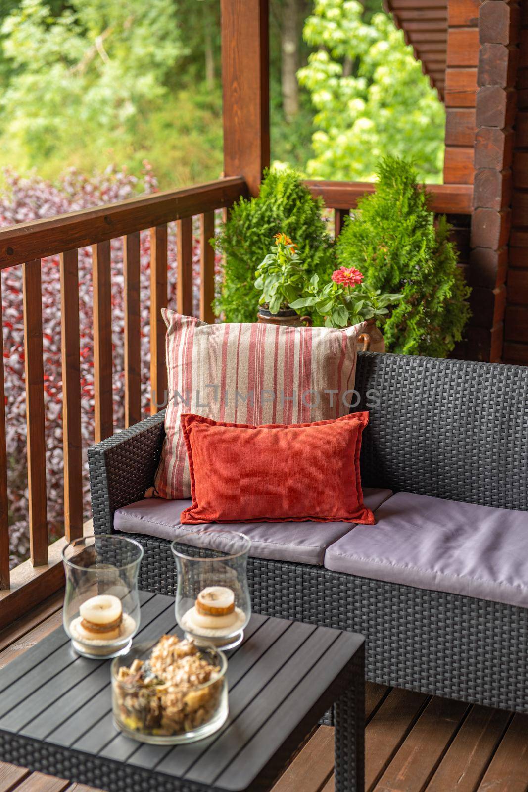 Cozy terrace with table and sofa at wooden cottage house surrounded by greenery and trees in countryside on cloudy summer day.