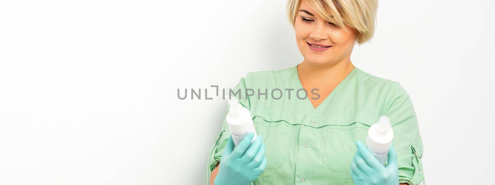 Cosmetics creams and skin care products in the hands of the female beautician smiling and standing over the white wall background. by okskukuruza