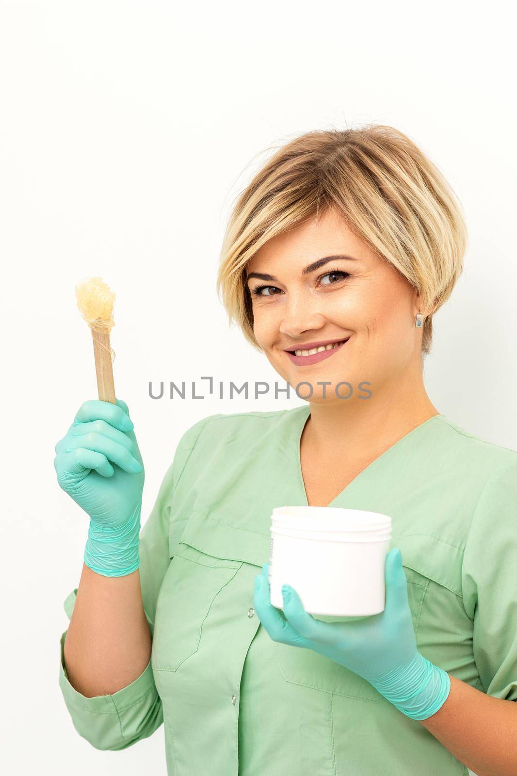 The master of sugar hair removal holds liquid yellow sugar paste, wax for depilation with the jar on a wooden stick on a white background. by okskukuruza