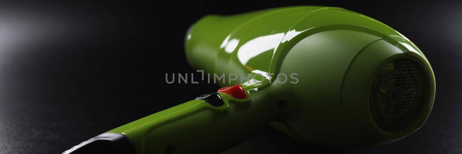 Close-up of green professional hairdryer device lay on black background, tool for beauty master. Equipment make hot air and dry hair. Beauty salon concept