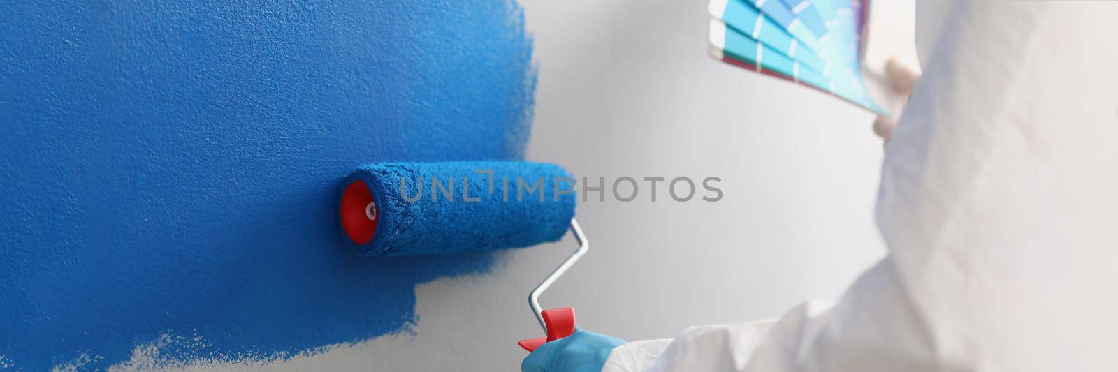 Painter with brush tool covered in blue colour painting wall, worker on site by kuprevich