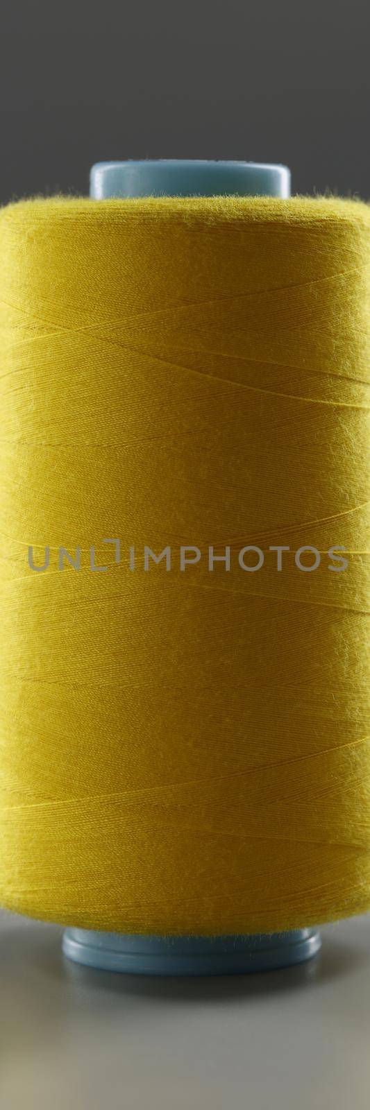 Yellow colour thread spool on grey background, yarn for sewing by kuprevich