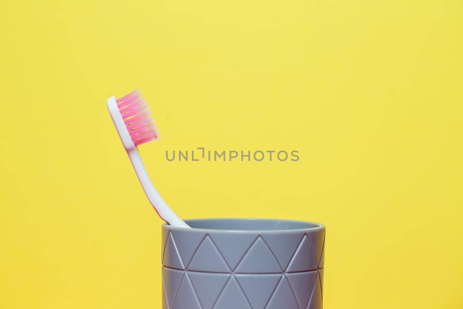 A pink toothbrush is standing in a gray glass. Dental care concept