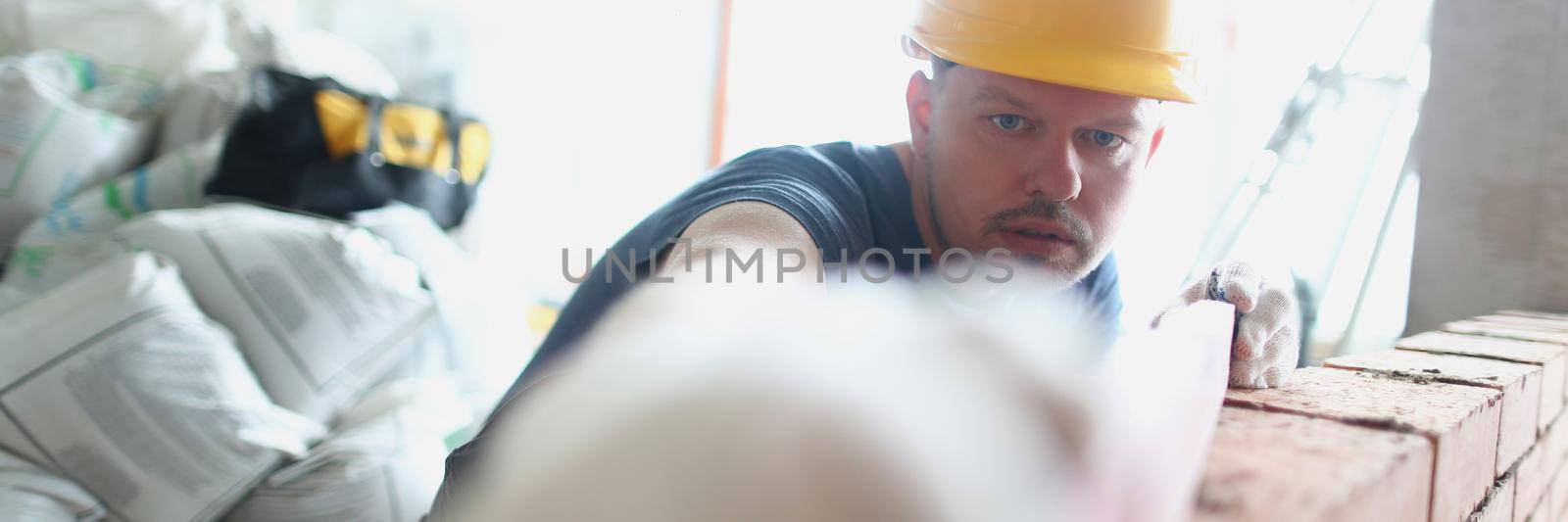Portrait of concentrated male builder measure distance with level equipment. Big concrete wall made of red bricks. Renovation, construction site concept
