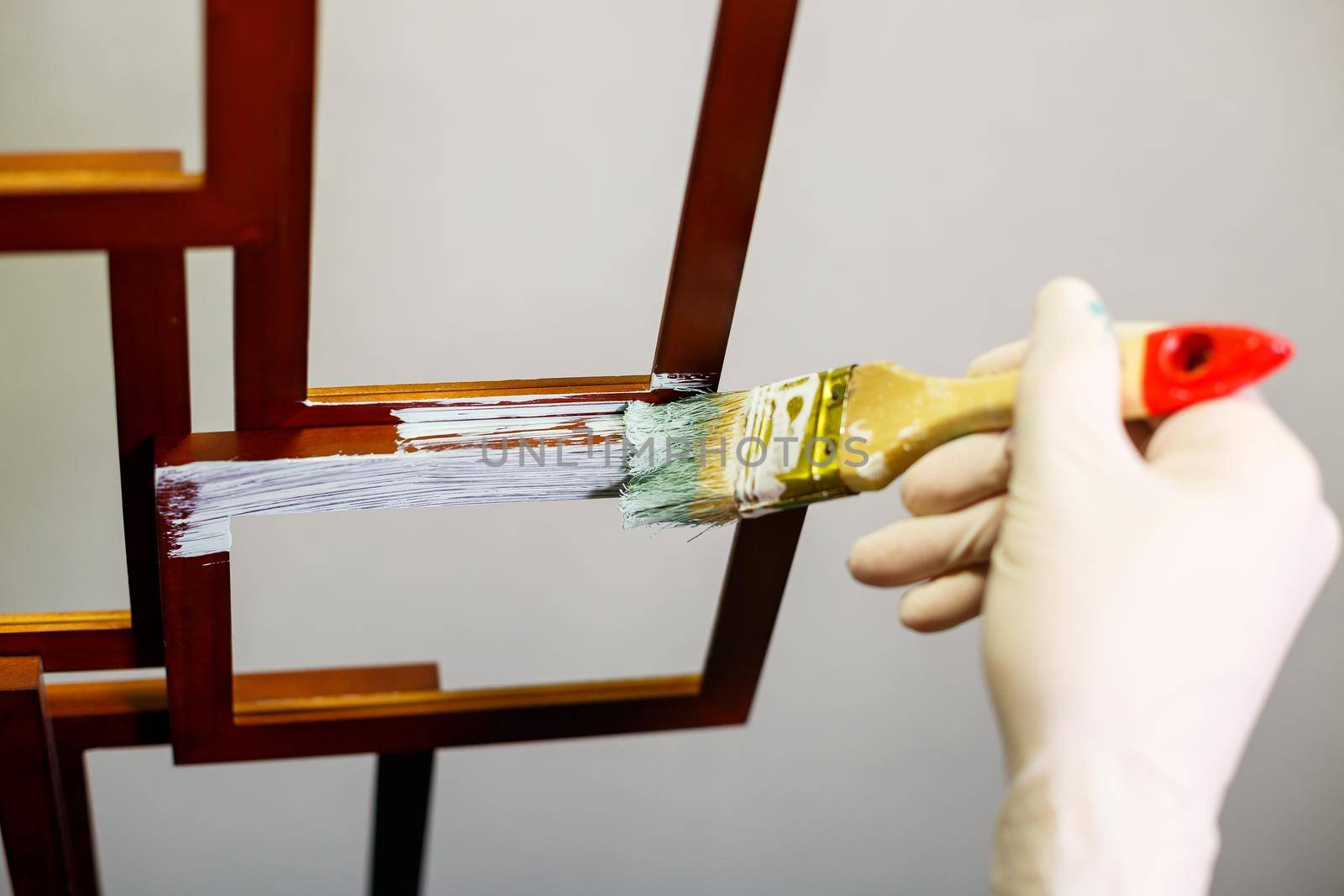 the master paints with a brush a wooden brown photo frame with light paint