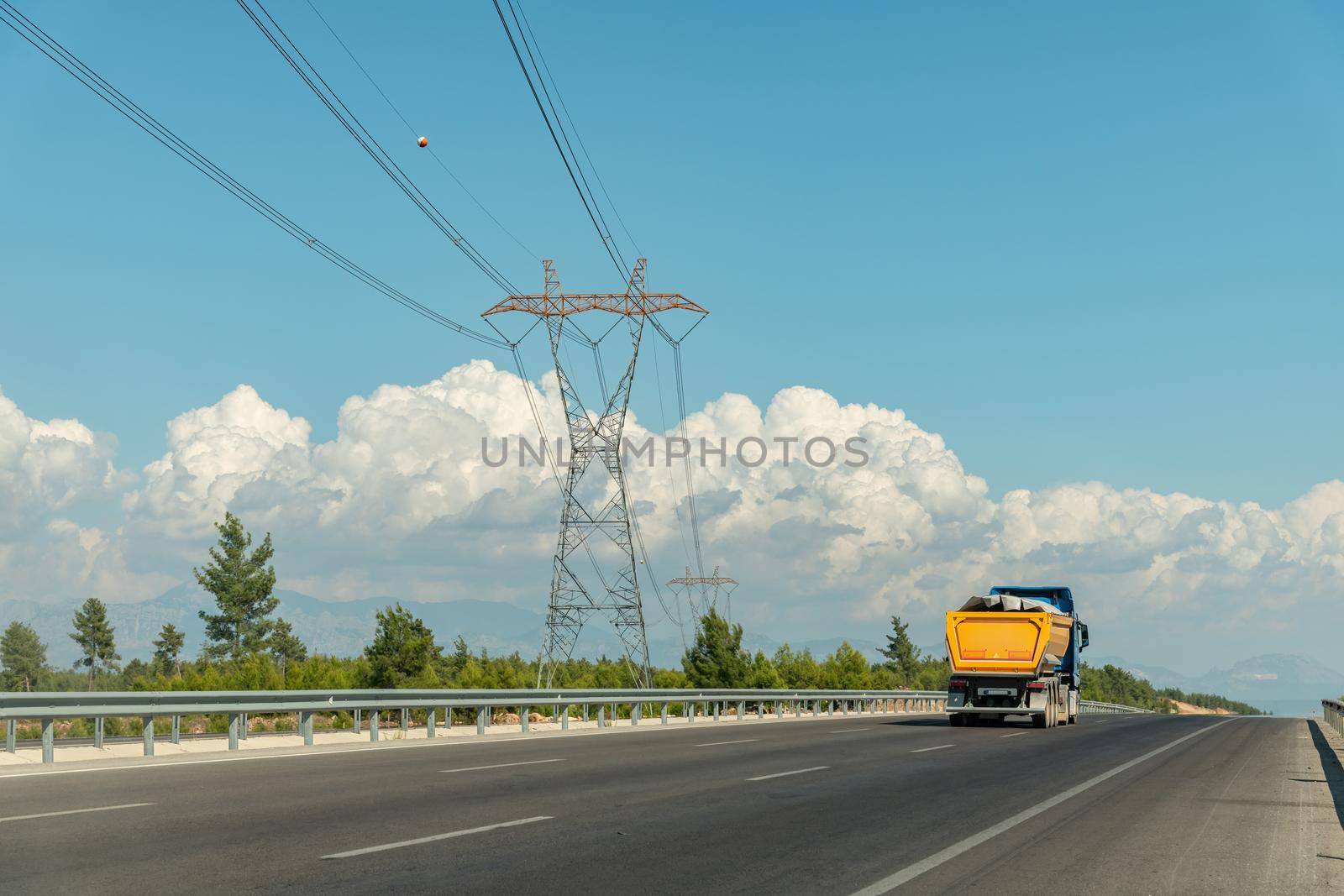 A truck going on a highway and a high-voltage power line on the side of the highway by Sonat