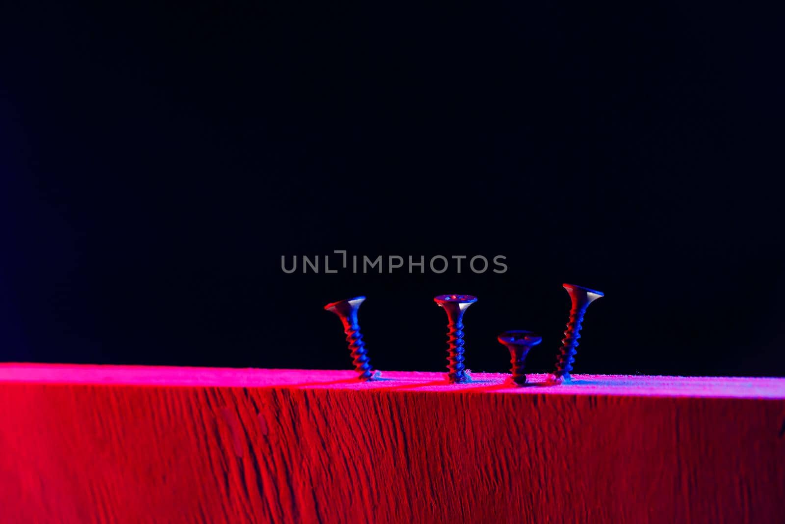 Screws screwed into a wooden beam in hard red light